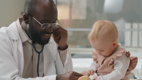 Pediatra-Negro-Usando-Estetoscopio-Y-Revisando-Al-Bebé-Caucásico